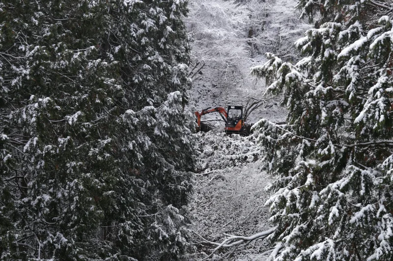 En grävmaskin arbetar längst in i en snötäckt skogsgata.